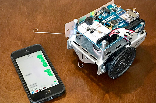 Small wheeled robot with exposed electronics next to a smartphone displaying a signal graph.